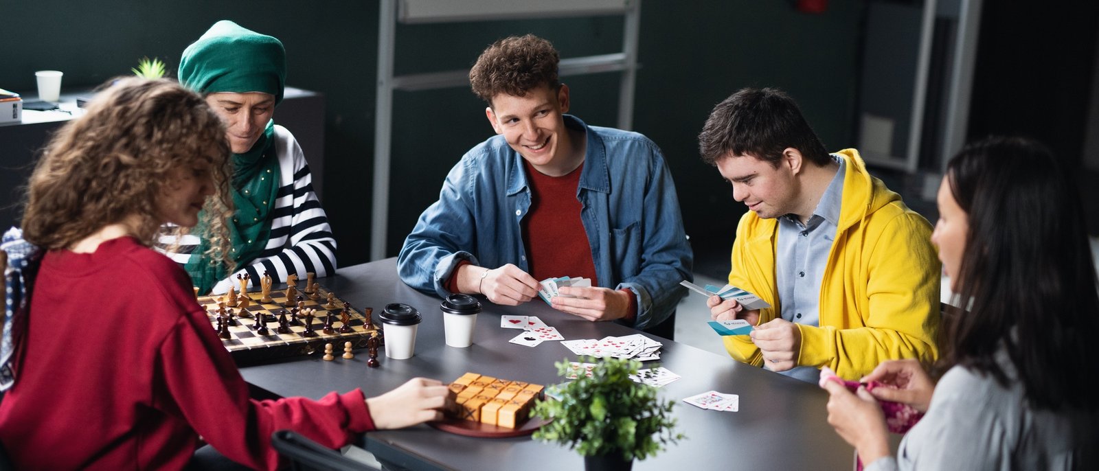 Group of people playing cards and board games in community center, inclusivity of disabled person