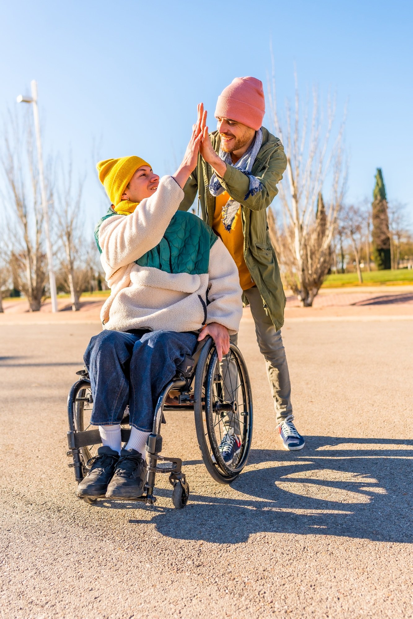 Young disabled woman in wheelchair giving high five to friend in park